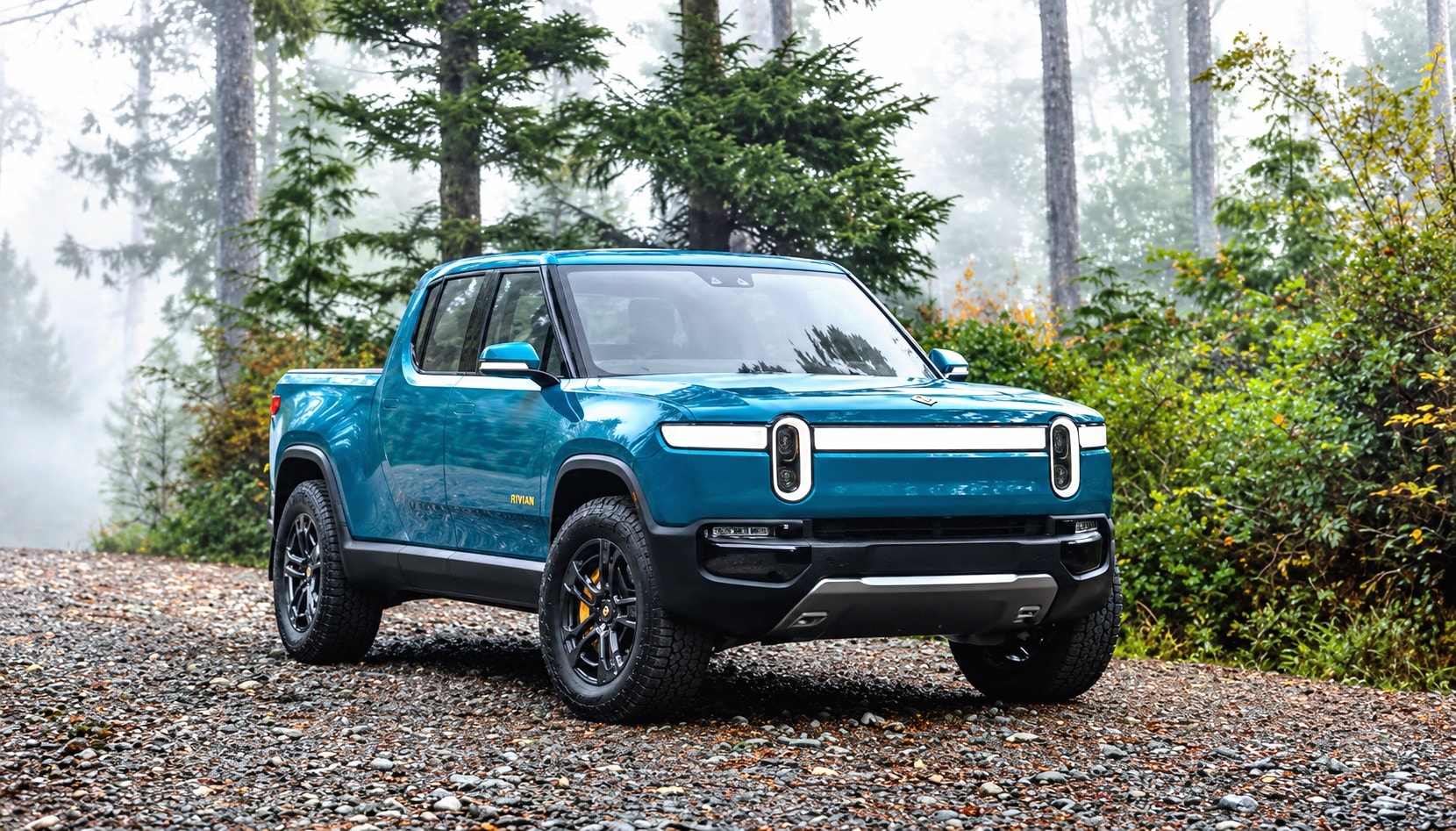 A blue electric pickup on a gravel track in a misty forest.