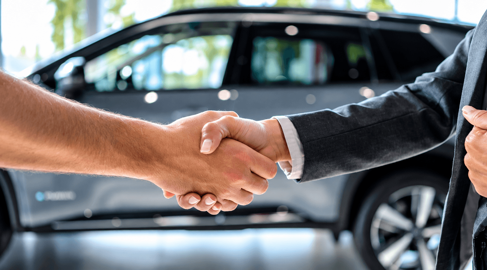Two people shaking hands in a showroom, in front of a dark SUV.