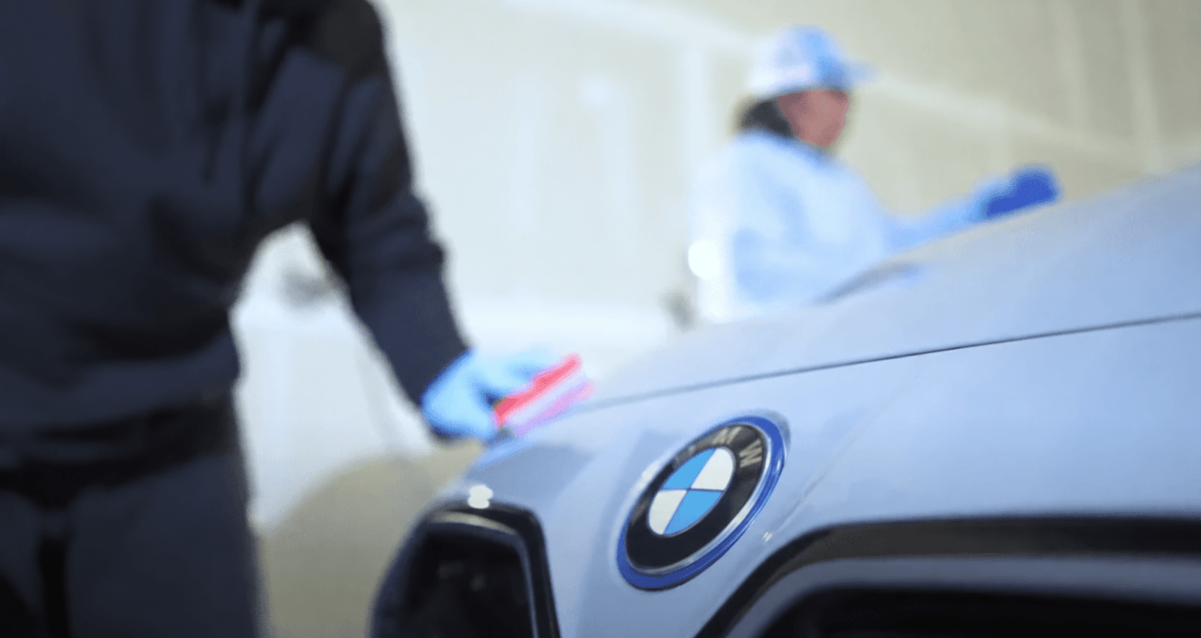 Two technicians going over a finished silver sedan with microfibre cloths.