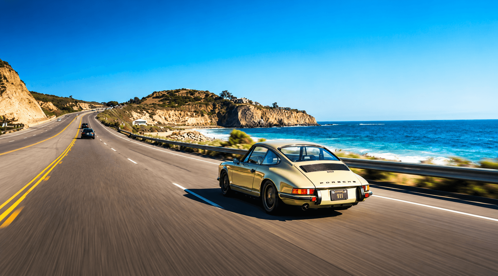 A classic Porsche 911 on the Pacific Coast Highway, the coastline and open ocean beyond it.